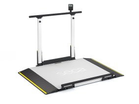 A flat, platform-style medical scale (seca XLine Hold) with yellow safety edges on the ramps, equipped with vertical support rails on both sides. A digital display unit (Basic Display) is mounted at the top of the rails, positioned centrally above the platform. The brand name 'seca' is printed in the center of the scale's surface.