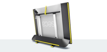 A large medical weighing platform with yellow safety edges (seca XLine Hold) is shown in a folded upright position, supported by its base. The back of the platform reveals the vertical support rails and a handle for easy transport. The brand name 'seca' is visible in reverse on the surface of the scale due to its folded position.